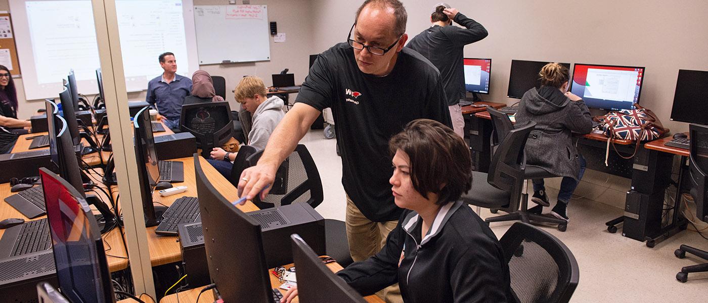 Instructor in an information security class pointing out important information on a computer screen to a student